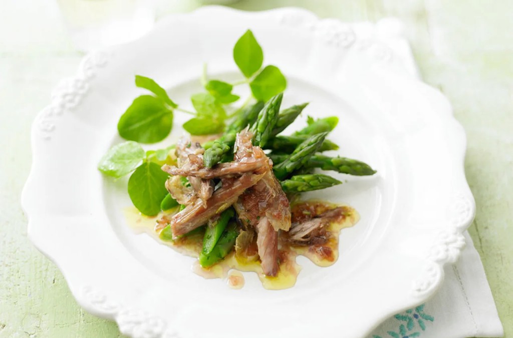 Elegant plated asparagus with shredded meat and herbs on a scalloped white plate