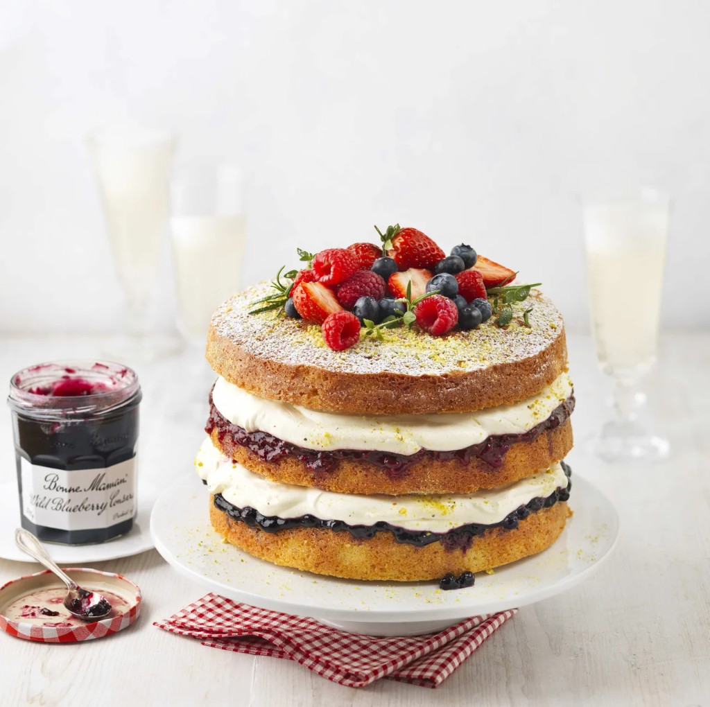Layered sponge cake with cream, berry jam, fresh berries, and conserve jar