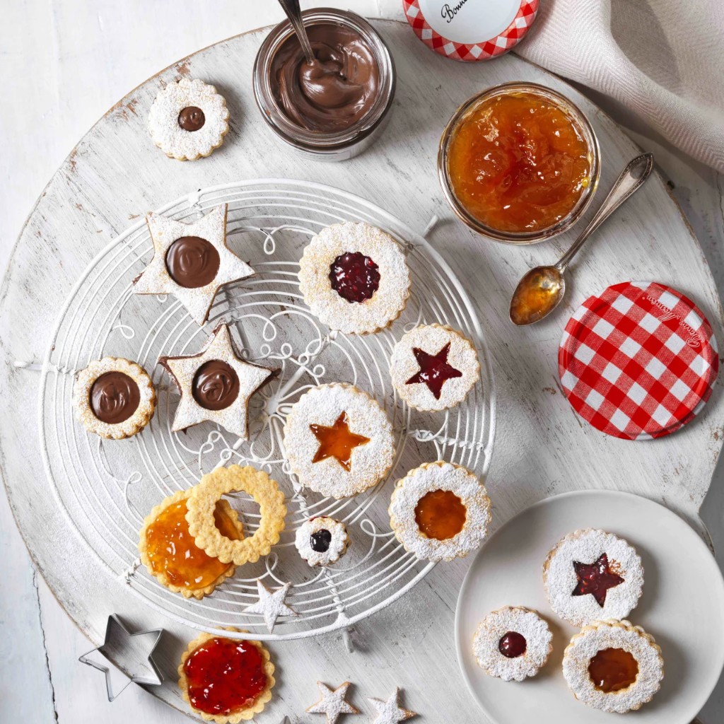 Overhead spread of jam-filled Linzer-style cookies on a cooling rack with jars